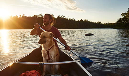 Hund sitzt mit seinem Herrchen in einem Boot auf einem See